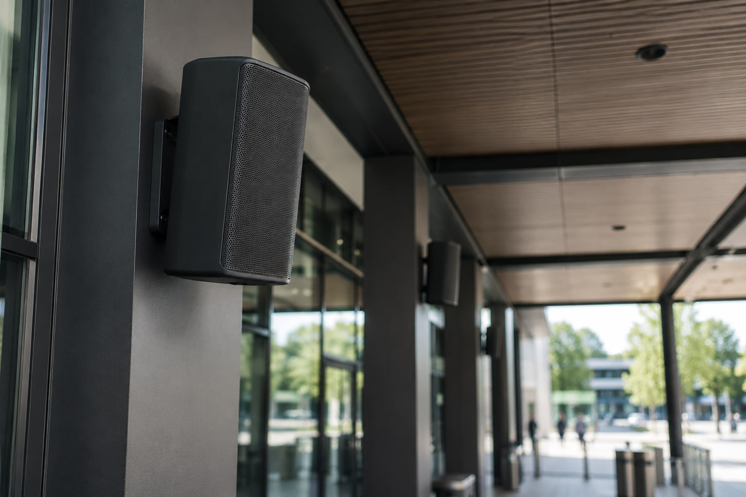 A weatherproof public address speaker mounted under the entrance canopy of a public building